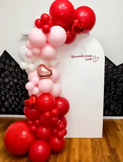 This balloon arrangement uses a simple white backdrop to make the red, pink, and white balloons stand out. The small heart-shaped foil balloon is a lovely detail in this romantic decor.