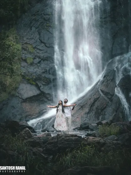 A breathtaking pre-wedding portrait with a couple embracing before a majestic waterfall.