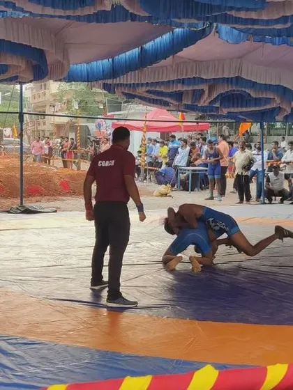 A modern wrestling match on a mat, showing the evolution of the sport. A referee watches closely as one wrestler works to pin his opponent.
