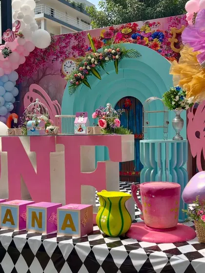 The full 'Onederland' stage for Ahana, with giant 'ONE' letters and a table filled with whimsical props. The checkerboard floor completes the classic Alice look.