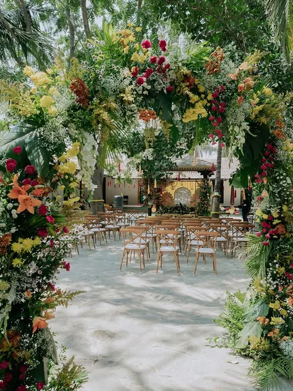 A grand floral archway, bursting with colorful flowers and tropical leaves, creates a stunning entrance for the Haldi ceremony.