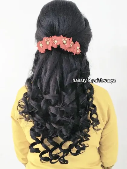 A half-up hairstyle with tight, defined curls. The floral hair accessory adds a pop of color to this fun and bouncy look.