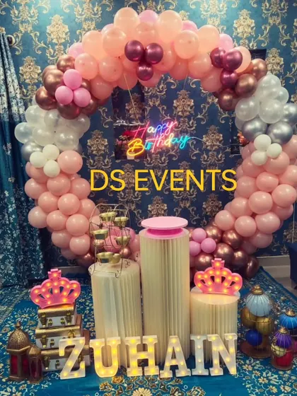 A royal-themed birthday in pink, rose gold, and silver. This setup includes a full circular balloon arch, a neon sign, and light-up props like crowns and the birthday boy's name in marquee letters.