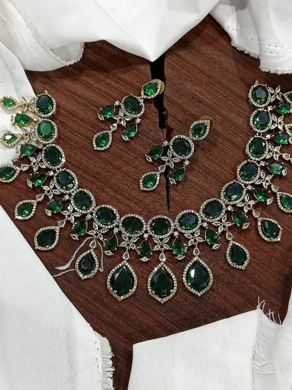 A stunning AD necklace set laid out to show its full design. This piece is available in multiple vibrant colors like ruby red, emerald green, pastel blue, and sapphire blue, featuring teardrop-shaped stones.