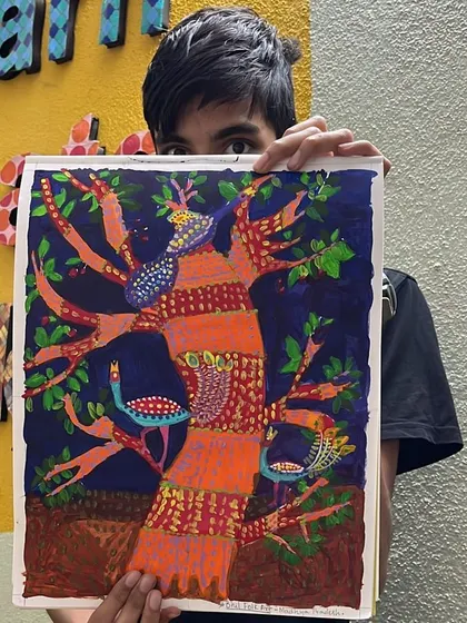 A student proudly but shyly shows his colorful Gond art painting, a tribal art form known for its intricate patterns filling a larger form.
