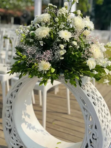 A close-up of the aisle decor for a white-themed wedding. Carved white stands hold lush bouquets of white chrysanthemums and baby's breath, creating an elegant and serene pathway for the bride.