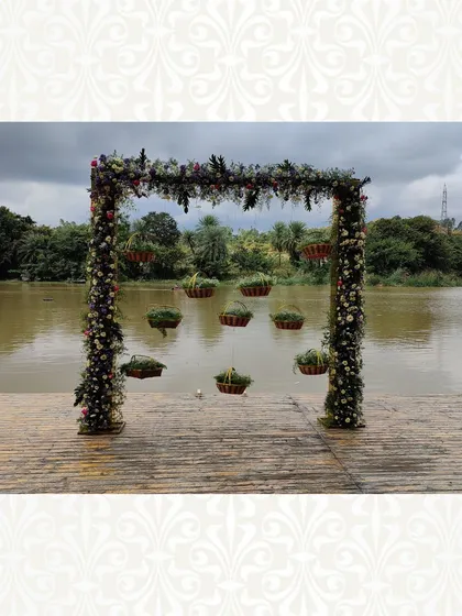 A beautiful floral arch set against a lake, with hanging flower baskets. This decor is designed to complement the natural beauty of the location.