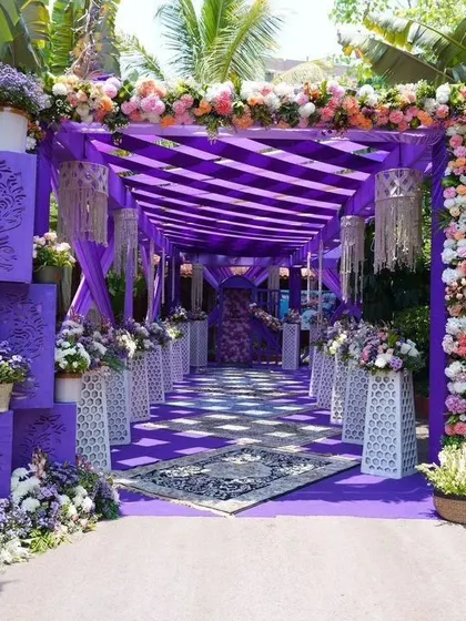 A bold and beautiful entrance decorated in shades of purple. The structured walkway is adorned with flowers and intricate panels, creating a royal and grand passage for guests.