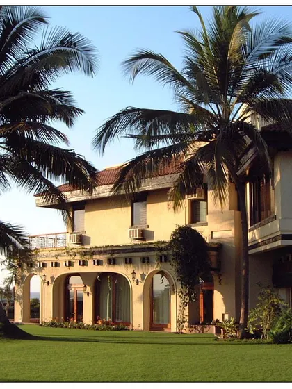 This sea-facing villa in Daman features traditional architectural elements like arched colonnades and a tiled roof, framed by beautiful palm trees that anchor it to its tropical location.