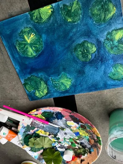 This image shows the work in progress of the koi pond painting. You can see my palette, brushes, and the initial layers of blue and green that form the base of the water scene.