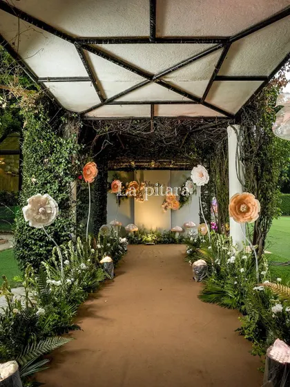 The pathway leading to the main event area was designed as an enchanted forest walk. Lined with faux greenery, oversized paper flowers, and tree stump accents, it created an immersive experience for guests.
