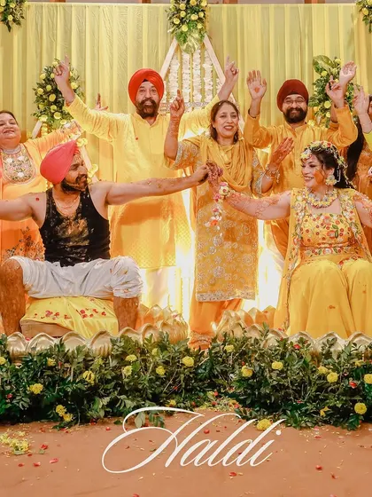 A group photo capturing the collective joy of the Haldi ceremony. The bride and groom are surrounded by their cheering family, all dressed in shades of yellow.