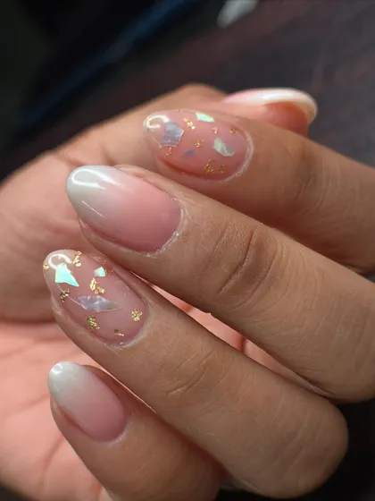 An inbuilt art design featuring a soft ombré base with delicate shell pieces and gold foil encapsulated within the nail.