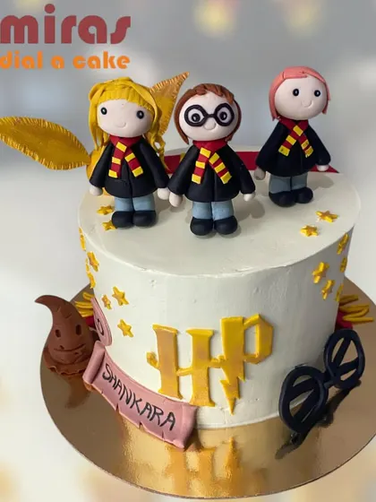 A magical Harry Potter cake featuring adorable, chibi-style figurines of Harry, Hermione, and Ron. The cake is decorated with the Sorting Hat, glasses, and the HP logo for a spellbinding birthday.