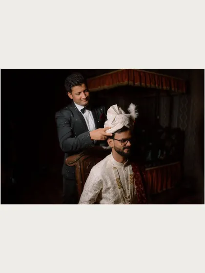 A candid moment of the groom getting ready, with a friend or family member helping him with his turban (pheta).