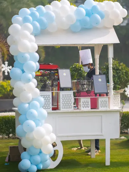 A food cart decorated with a blue and white balloon arch, ready to serve treats at the winter-themed outdoor party.