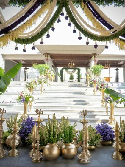 The grand steps of the venue are lined with brass vases filled with florals and traditional lamps, creating a beautiful and auspicious pathway for the wedding.