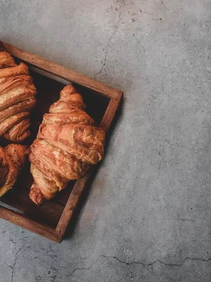 Flaky, buttery croissants captured in a moody, rustic style. The dark, textured background and top-down angle highlight the pastry's layers, creating an artisanal feel.