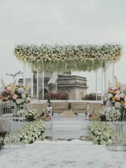 A stunning floral mandap with a floating canopy of white flowers, perfectly framing the Gateway of India in the background. This design blends iconic scenery with luxurious decor for a truly unique Mumbai wedding.