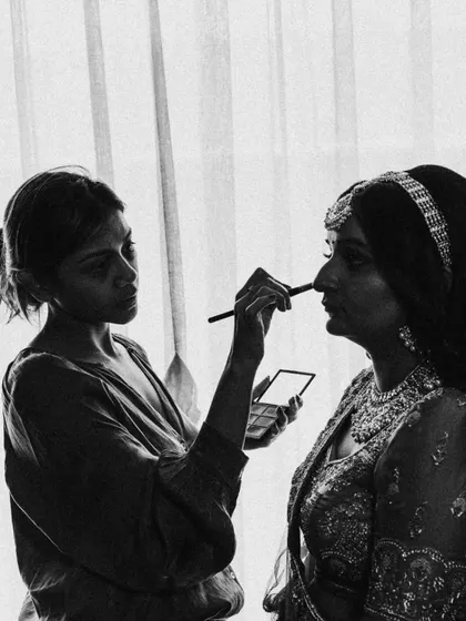 Another angle of Maitri's makeup session, this time in black and white, focusing on the artist's concentration and the bride's calm presence.