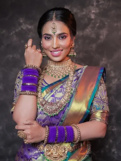 A joyful portrait of a model in a vibrant purple silk saree. Her bright smile and confident pose perfectly showcase the beauty of the traditional attire and gold jewelry.