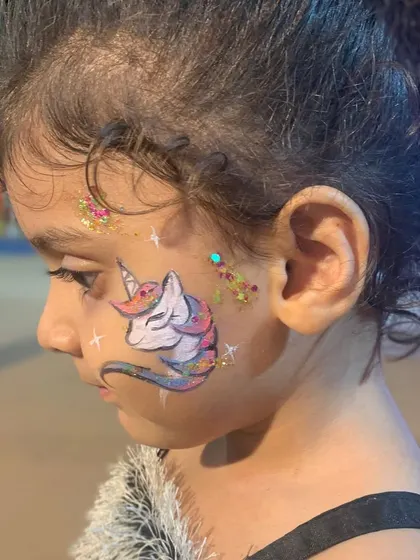 A close-up of a rainbow unicorn design on a young child, showing the blend of colors and glitter.