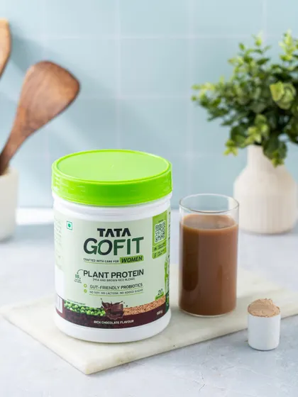 A kitchen-setting shot for a women's plant protein product. The styling with kitchen utensils and a prepared shake suggests ease of use in a daily routine.