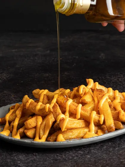 This action shot captures cheese and sauce being drizzled over fries. The motion and the glistening sauce make a simple side dish look incredibly decadent and appealing.