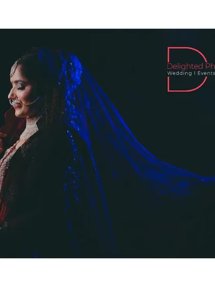 An ethereal bridal portrait with a flowing blue veil against a black background. The dramatic lighting and movement create a stunning, almost magical effect.