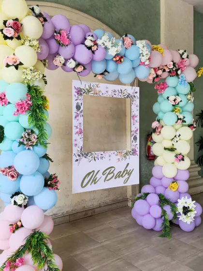 A beautiful "Oh Baby" photo frame surrounded by a pastel rainbow balloon arch. The arch is decorated with delicate flowers, making it perfect for a spring or garden-themed baby shower.