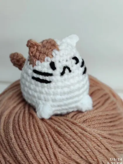 A chubby cat plushie sitting on a ball of yarn.