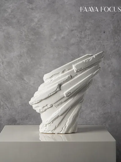 This abstract white sculpture appears like a piece of carved stone, with sharp angles and deep ridges. It is an object of quiet strength, perfect for adding a touch of brutalist elegance to a minimalist space.