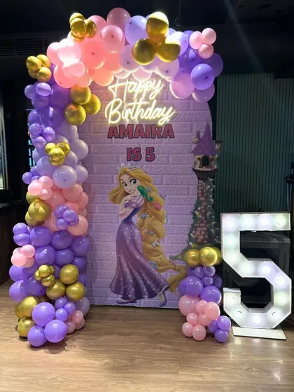 Let your hair down! This Rapunzel-themed decoration for Amaira's 5th birthday featured a tower backdrop and a beautiful balloon arch in shades of purple, pink, and gold. The large, illuminated '5' made the princess's day shine even brighter.