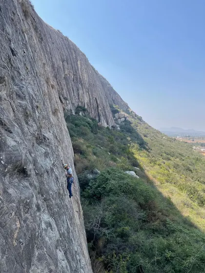 A wide shot showing a climber high up on the massive rock face of Varlakonda. The scale of the cliffs here is truly impressive.