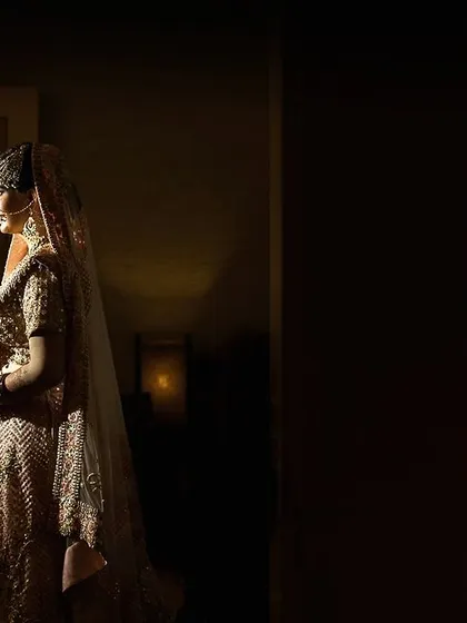 A profile shot of the bride, her form illuminated against a dark, moody background. This elegant portrait highlights her silhouette and the details of her attire.