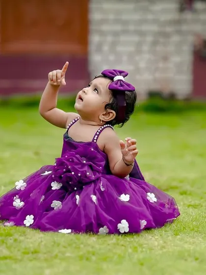 This little angel in a purple dress is pointing up at the sky, full of wonder and curiosity during her outdoor photoshoot.