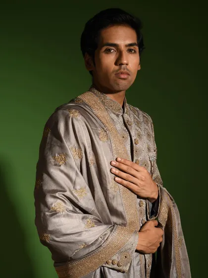 My steel grey raw silk sherwani is an ideal choice for a groom seeking a sophisticated and modern color palette. The ensemble includes a matching stole with detailed borders, adding a layer of elegance.