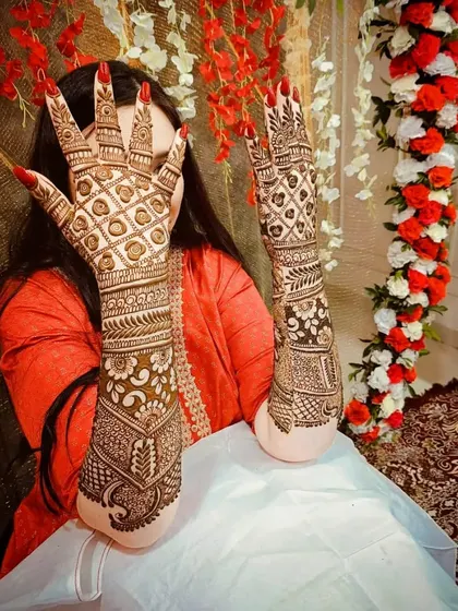 A beautiful shot of a bride displaying her intricate back-hand mehandi against a festive floral backdrop.