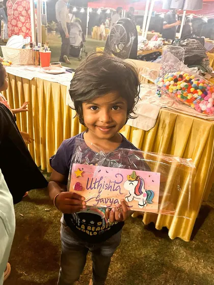 A little girl with a huge smile, holding the unicorn nameplate she painted.
