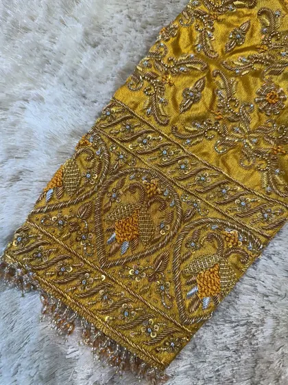 An extreme close-up of the sleeve embroidery on the mustard yellow blouse, showing the detailed craftsmanship of the zardosi and sequin work.