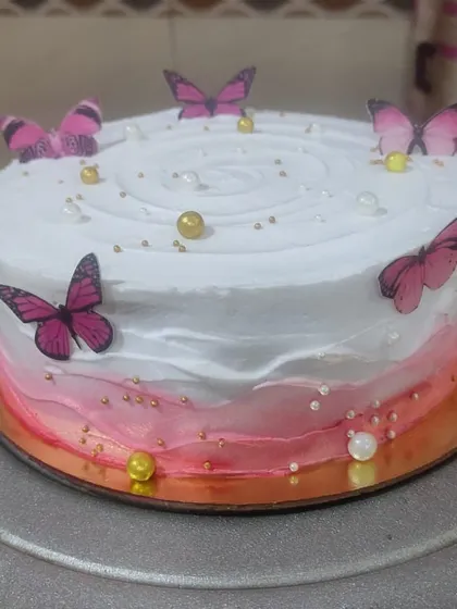 This butterfly-themed cake features a soft pink and white ombre design. It's decorated with delicate edible butterflies and golden pearls for a touch of magic.