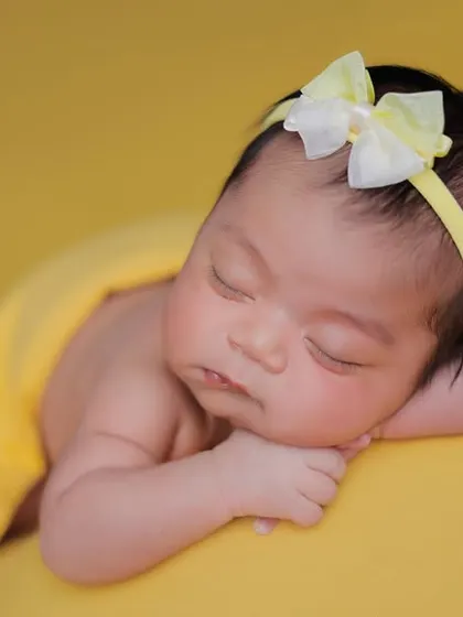 A close-up of a sleeping newborn against a bright yellow backdrop, showing the delicate details of their face.