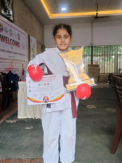 This young warrior proudly displays her trophy and certificate after a successful competition. Her achievement reflects her dedication to the art of karate.