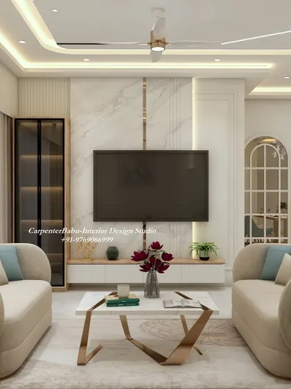 A modern living room with a floating TV unit set against a white marble panel. The curved sofas and metallic-finish coffee table add a soft, luxurious touch to the minimalist aesthetic.