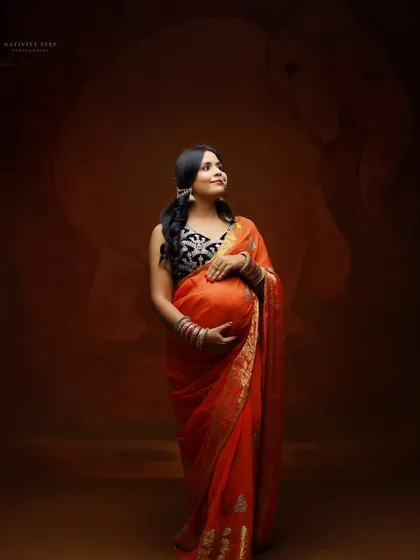 A beautiful three-quarter portrait of an expecting mother in a saree, gently holding her bump. The studio lighting enhances the rich colors of her attire.