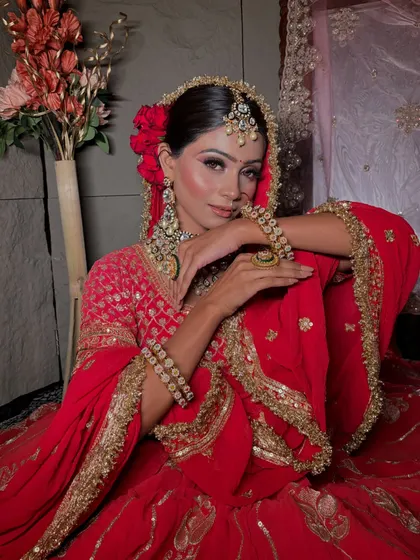 A full-length view of a classic red bridal lehenga look. The makeup is designed to be regal and timeless, with a floral bun adding a touch of softness.