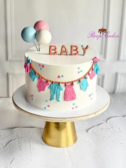 A sweet celebration for the tiniest bundle of joy. This adorable baby shower cake is decorated with a clothesline of fondant baby clothes, pastel polka dots, and balloon toppers.