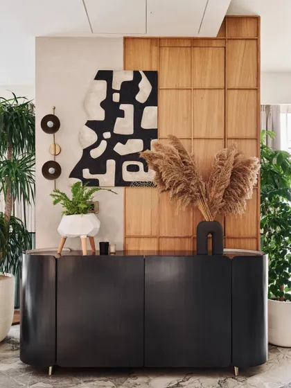 A curved black console table stands against a backdrop of wood paneling and textured paint. This corner is styled with pampas grass and abstract art, showcasing the home's focus on natural textures and modern forms.