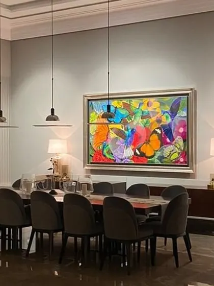 The dining area in the farmhouse is defined by a vibrant, colorful painting. The long table and comfortable chairs are designed for large family gatherings, making it a hub of connection and shared meals.