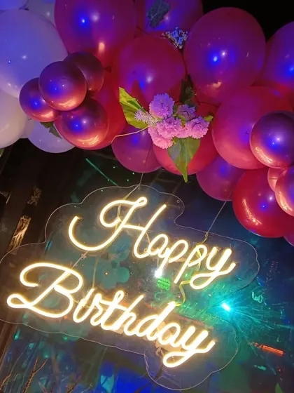 A close-up of the "Happy Birthday" neon sign, showing the floral details tucked into the balloon arrangement.